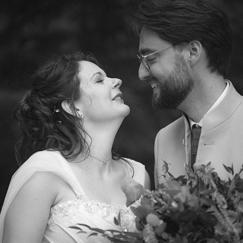 A laughing couple stands close together in a romantic black and white moment surrounded by foliage.