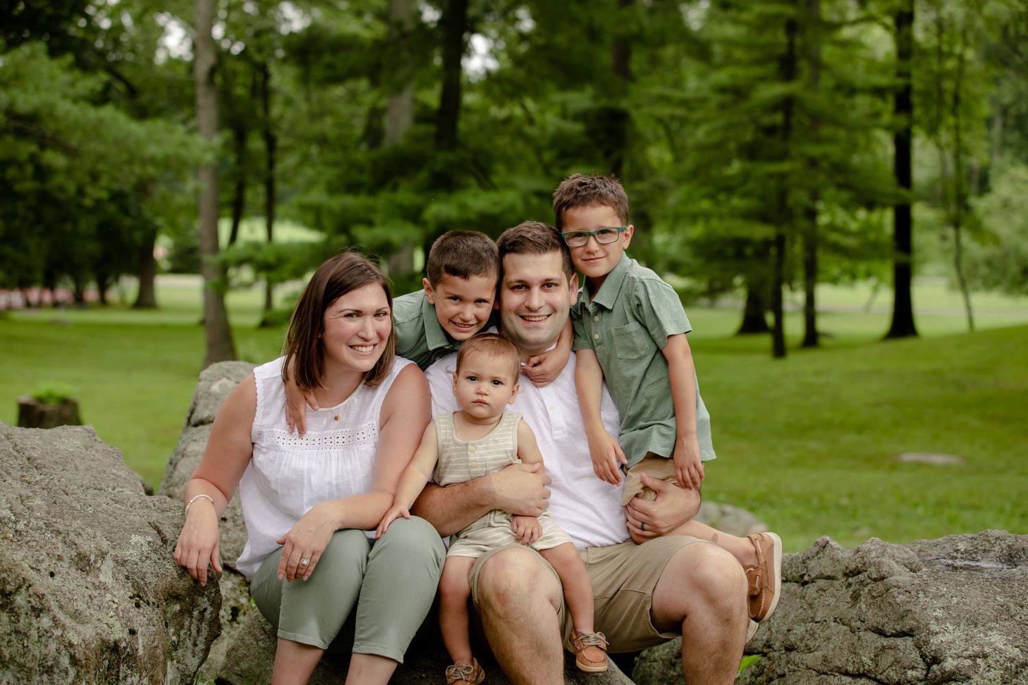 Family enjoying outdoor picnic time together on large rocks in a lush green park setting.