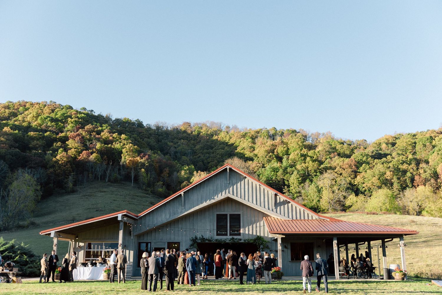 Group photo at rustic mountain wedding venue with trees and modern buildings in background.