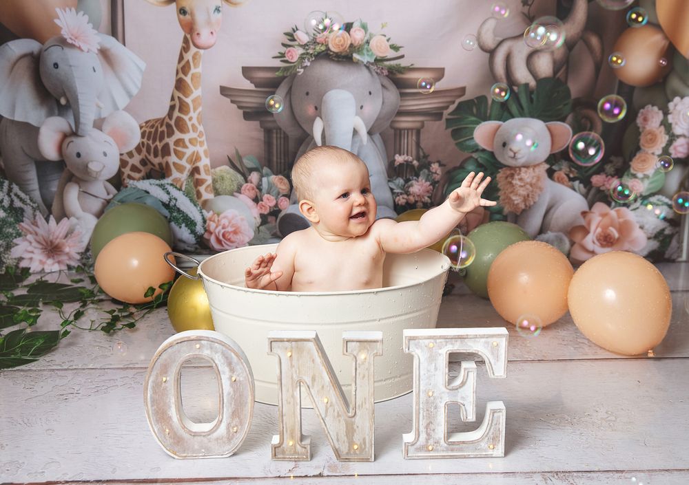 Baby portrait session with peach-colored balloons, bunny plush toys, and wooden ONE letters in a rustic setting.