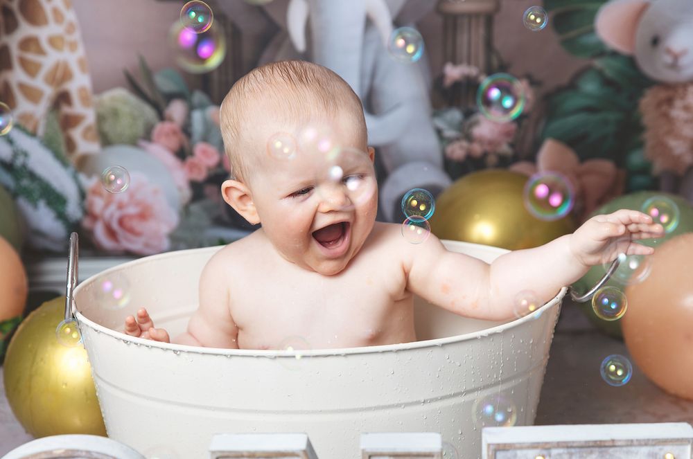 A joyful baby sits in a white wash basin surrounded by colorful balloons and bubbles during bath time. During photoshoot in London, Bexley.