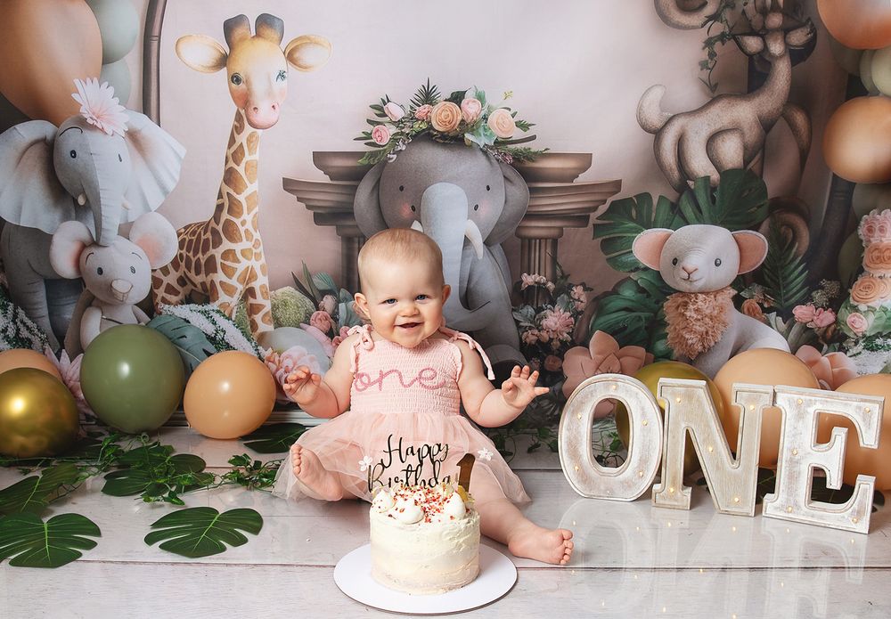 A rustic cake smash photo collage with stuffed animals, green foliage, and 'ONE' text decor in neutral tones. During photoshoot in London