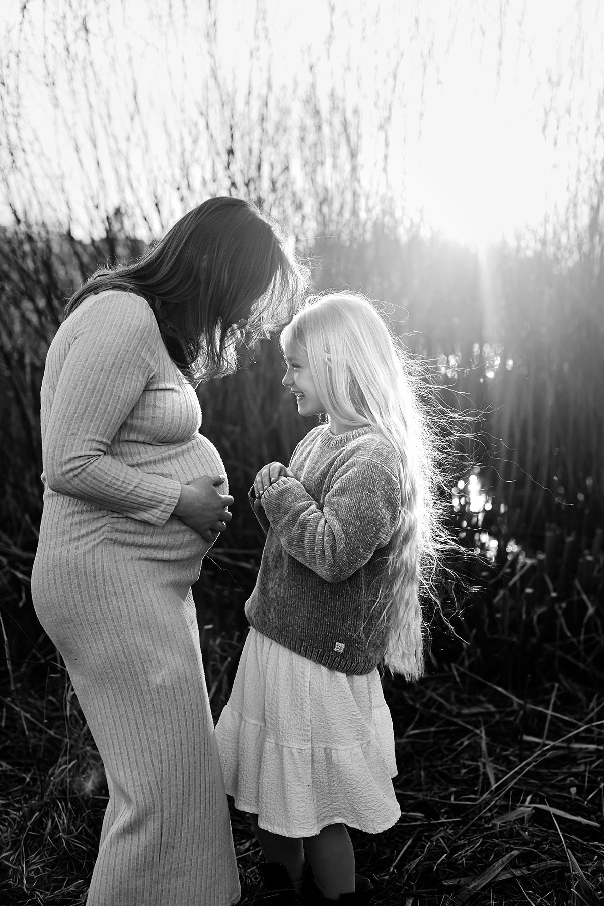 Svartvit gravidfoto med mamma tillsammans med sin dotter, mamman håller om sin mage och de ser in i varandras ögon och skrattar. Lets Bloom