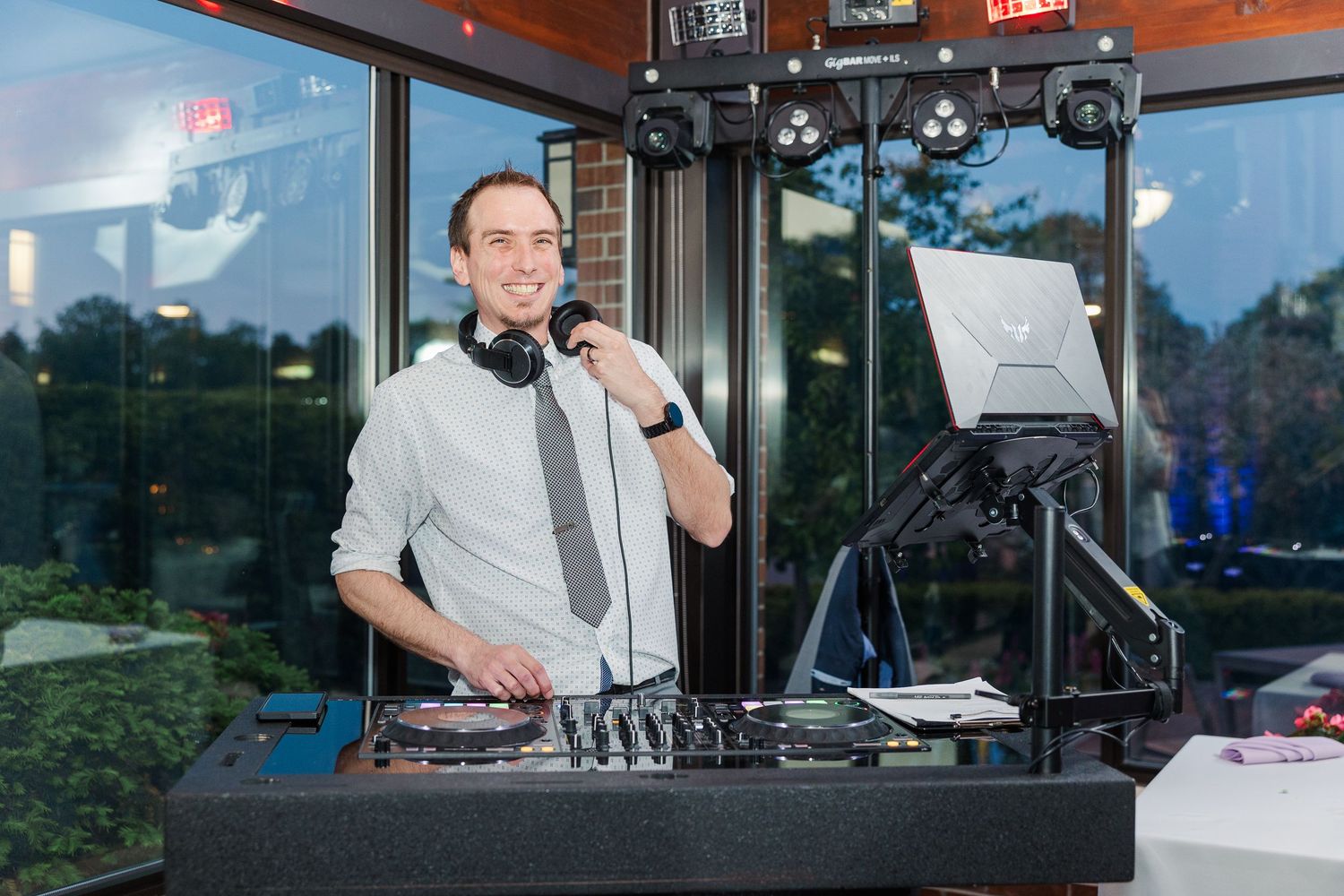 A DJ performs at an event using professional equipment and wearing a white shirt with black tie.