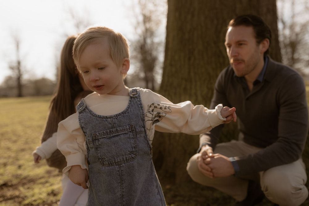 Candid outdoor moment of toddler in denim overalls with caregiver at golden hour.
