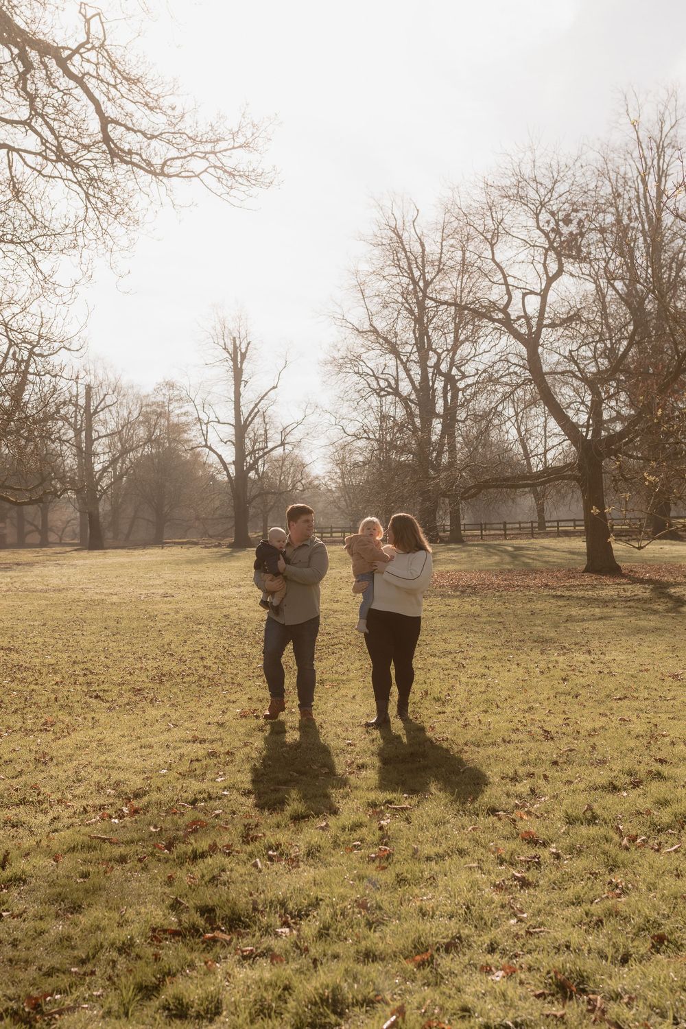A group gathers in a sunlit meadow on a misty morning with bare trees in the background.