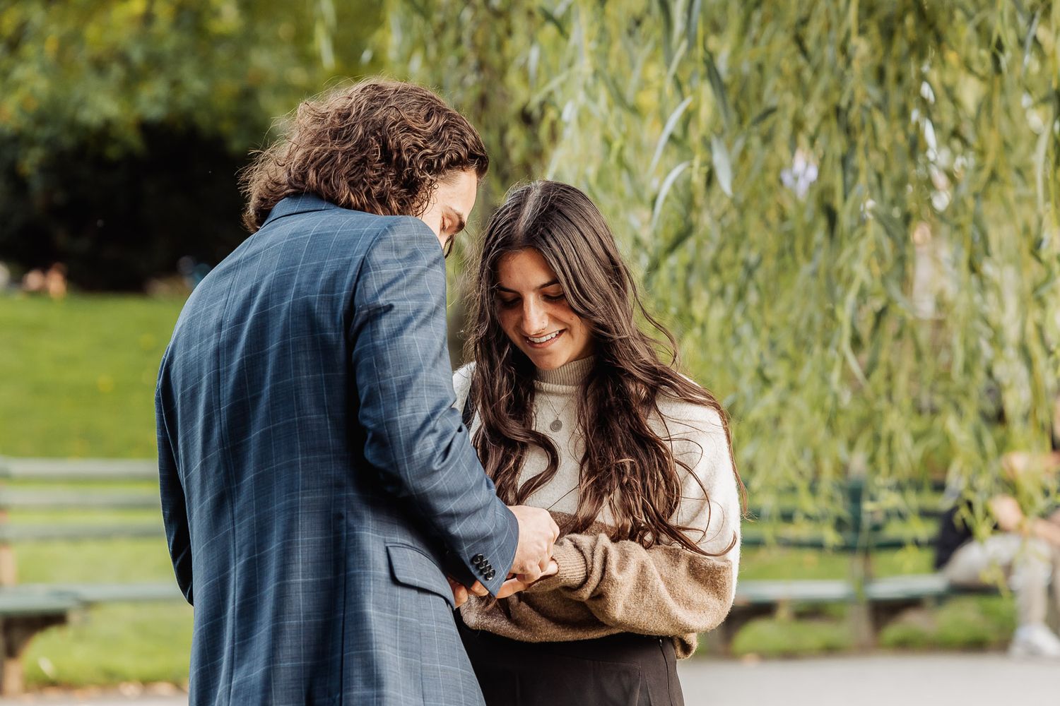Couple sharing intimate moment under willow tree in park setting.