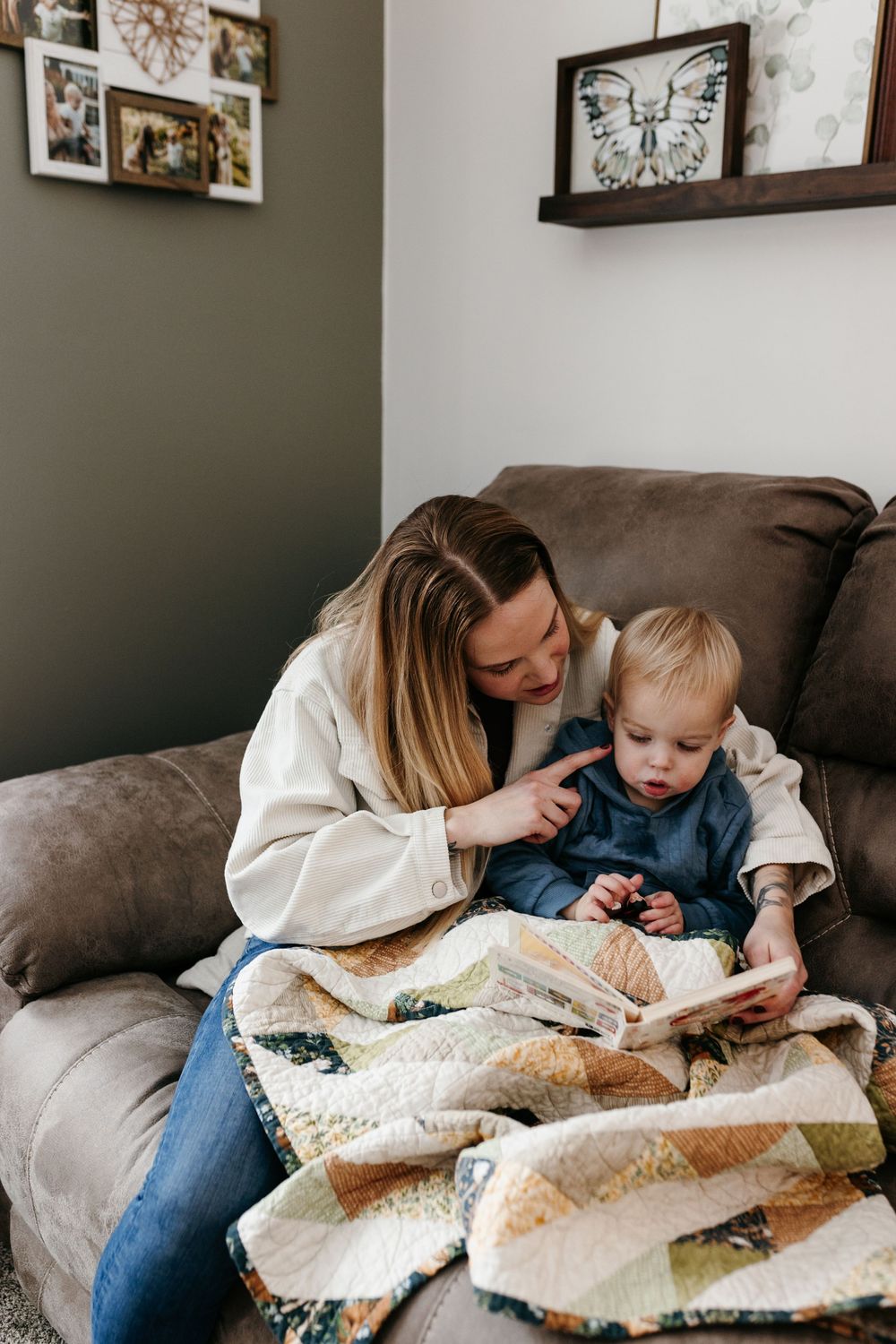 A parent and toddler share a tender moment reading together under a cozy patchwork quilt on a brown sofa.