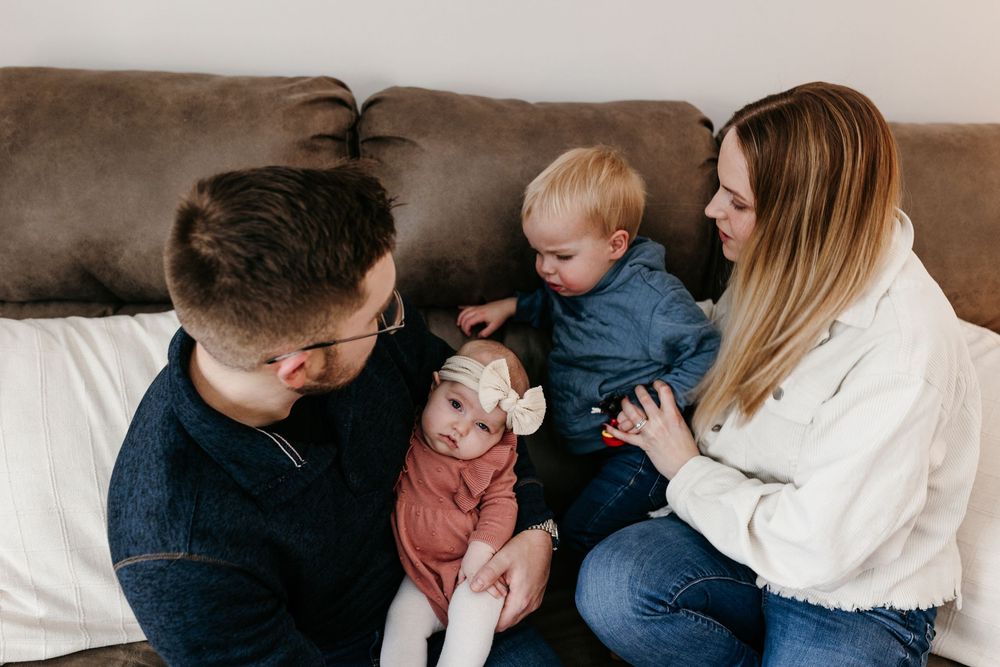 A happy family sits together on a gray couch, sharing a tender moment in their casual home setting.