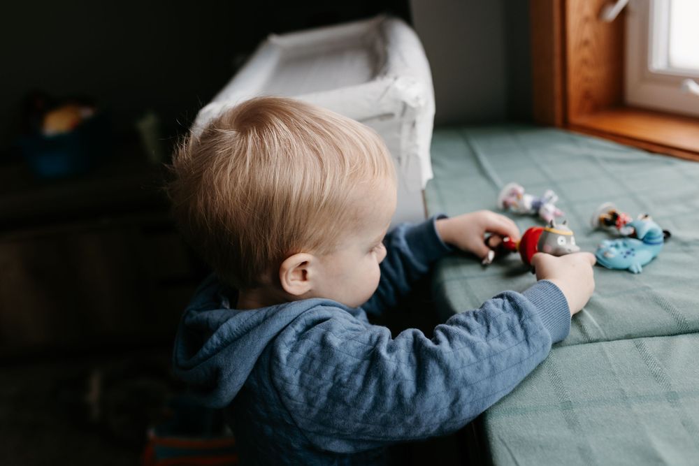 Small child in denim shirt plays with toys on a turquoise surface near a window.
