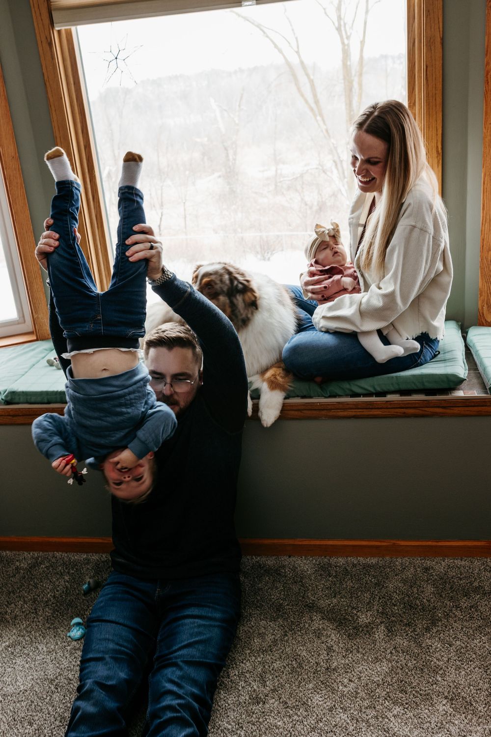 A family relaxes by a window on a winter day with their dog while playing and spending time together.