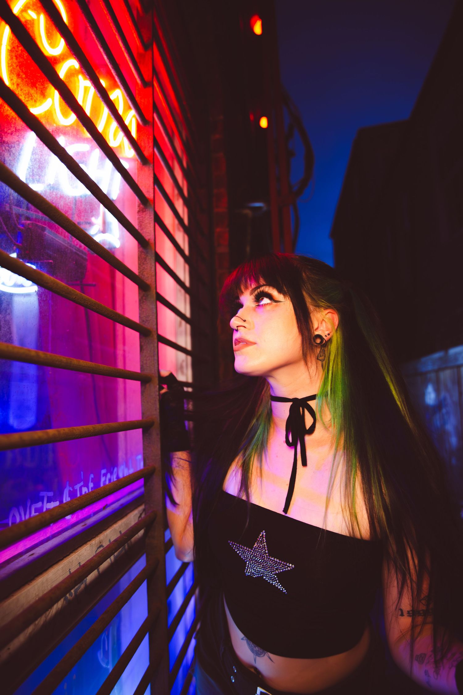 Close up beauty shot featuring green hair highlights and dark eye makeup against a graffiti wall in dim lighting.