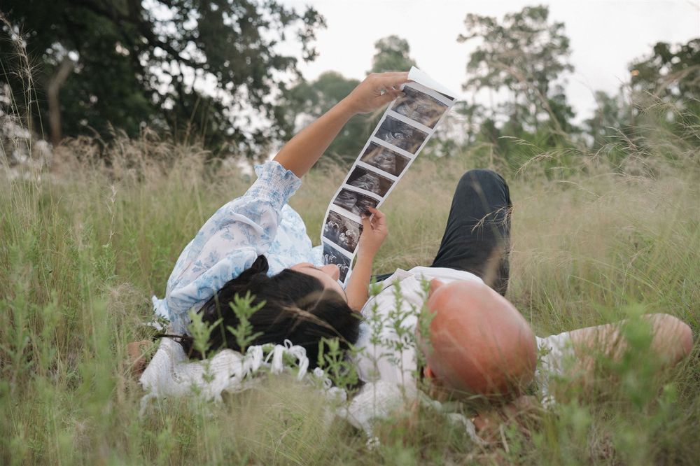 Someone lying in a meadow of tall grass holding up a film strip or photo negatives against the cloudy sky.