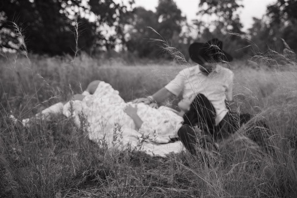 A black and white photo shows a couple resting in a grassy field on a summer afternoon.