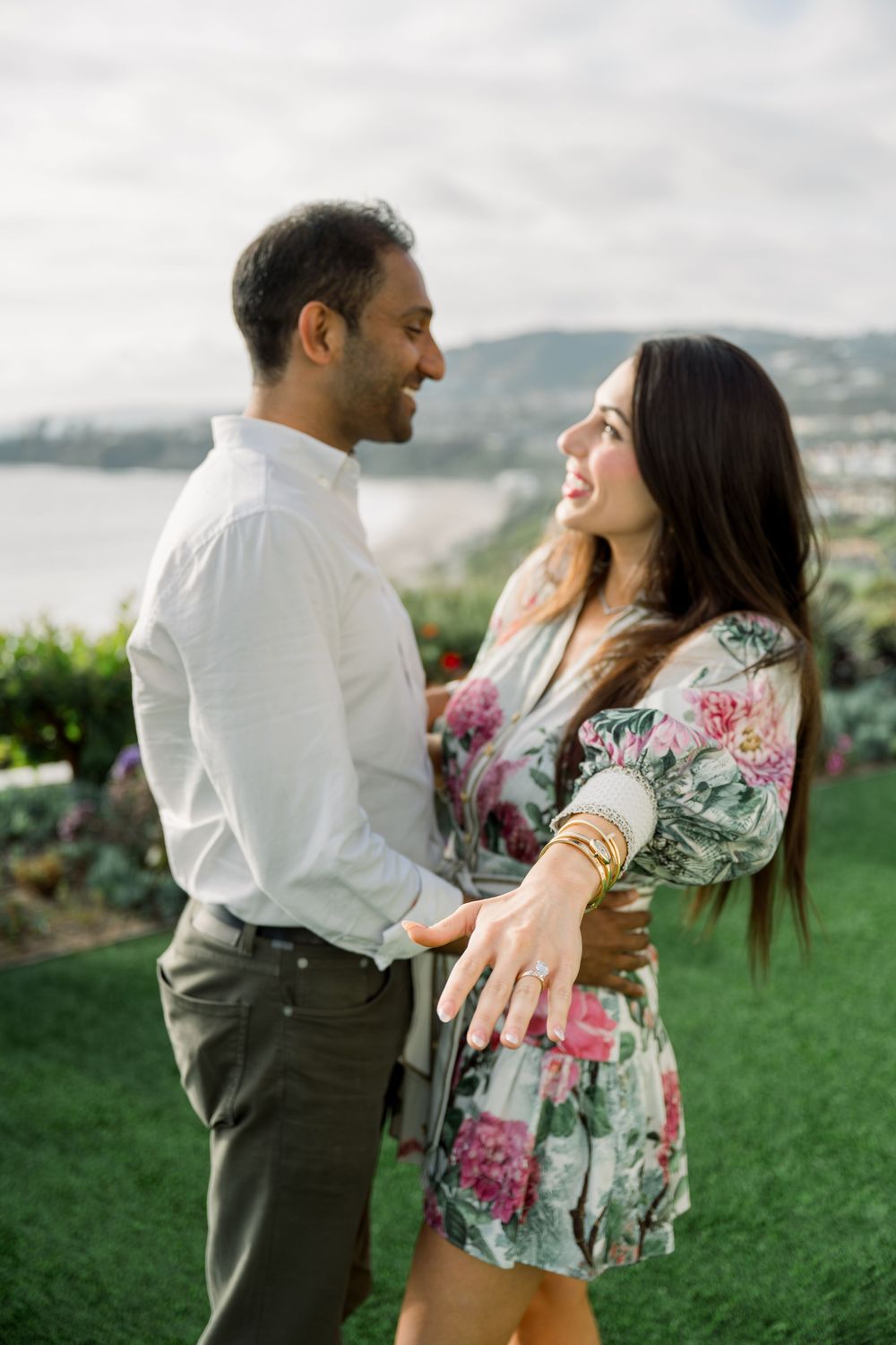 Happy couple sharing a joyful moment outdoors on a grassy lawn overlooking a waterfront landscape.