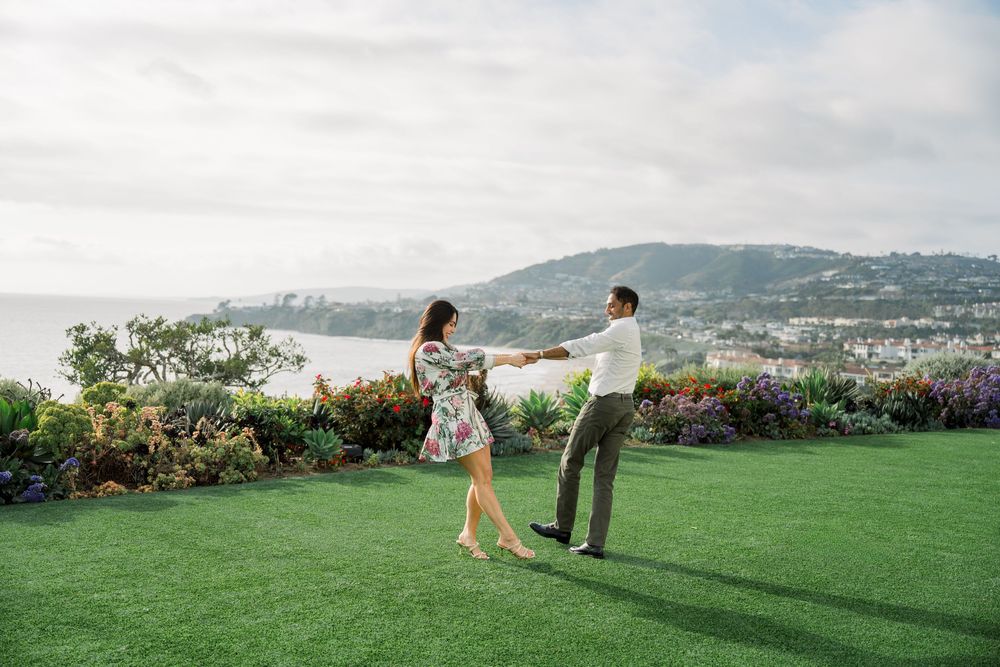 Couple stands on lush green lawn overlooking coastal cliffs and ocean views during romantic photoshoot.