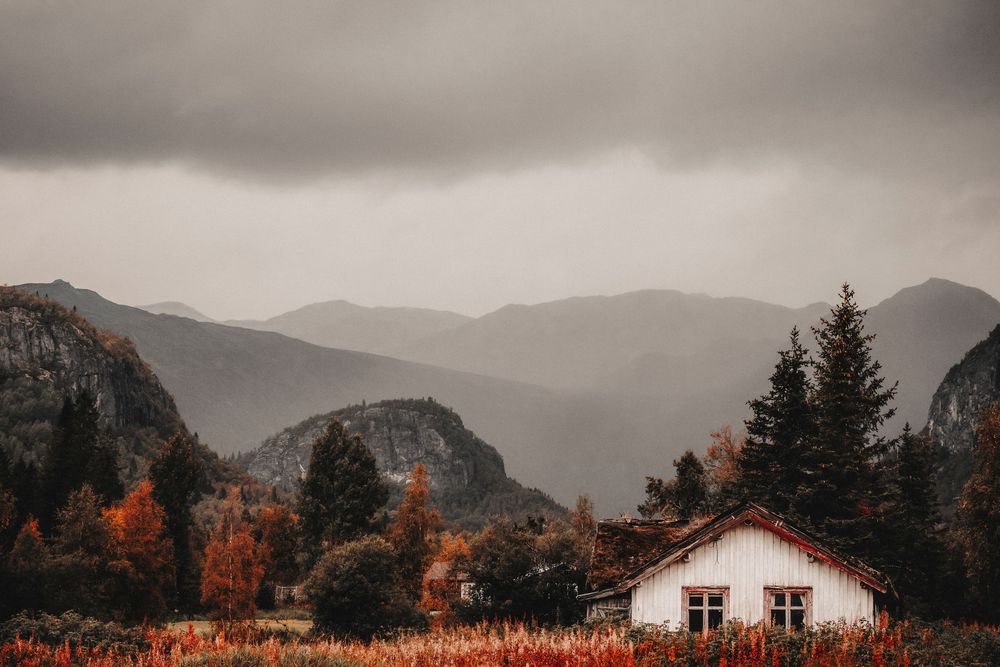 A white cottage nestled in mountain landscape with autumn foliage and moody overcast skies.