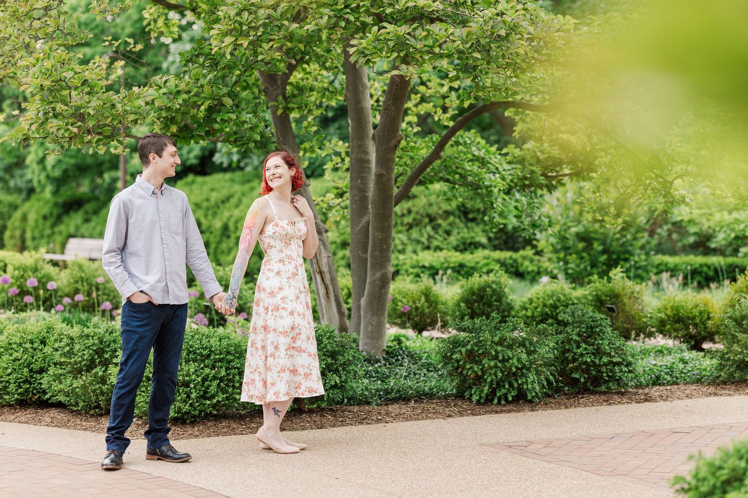 A couple walks hand in hand along a garden path surrounded by lush greenery and trees on a sunny day at Cantigny Park