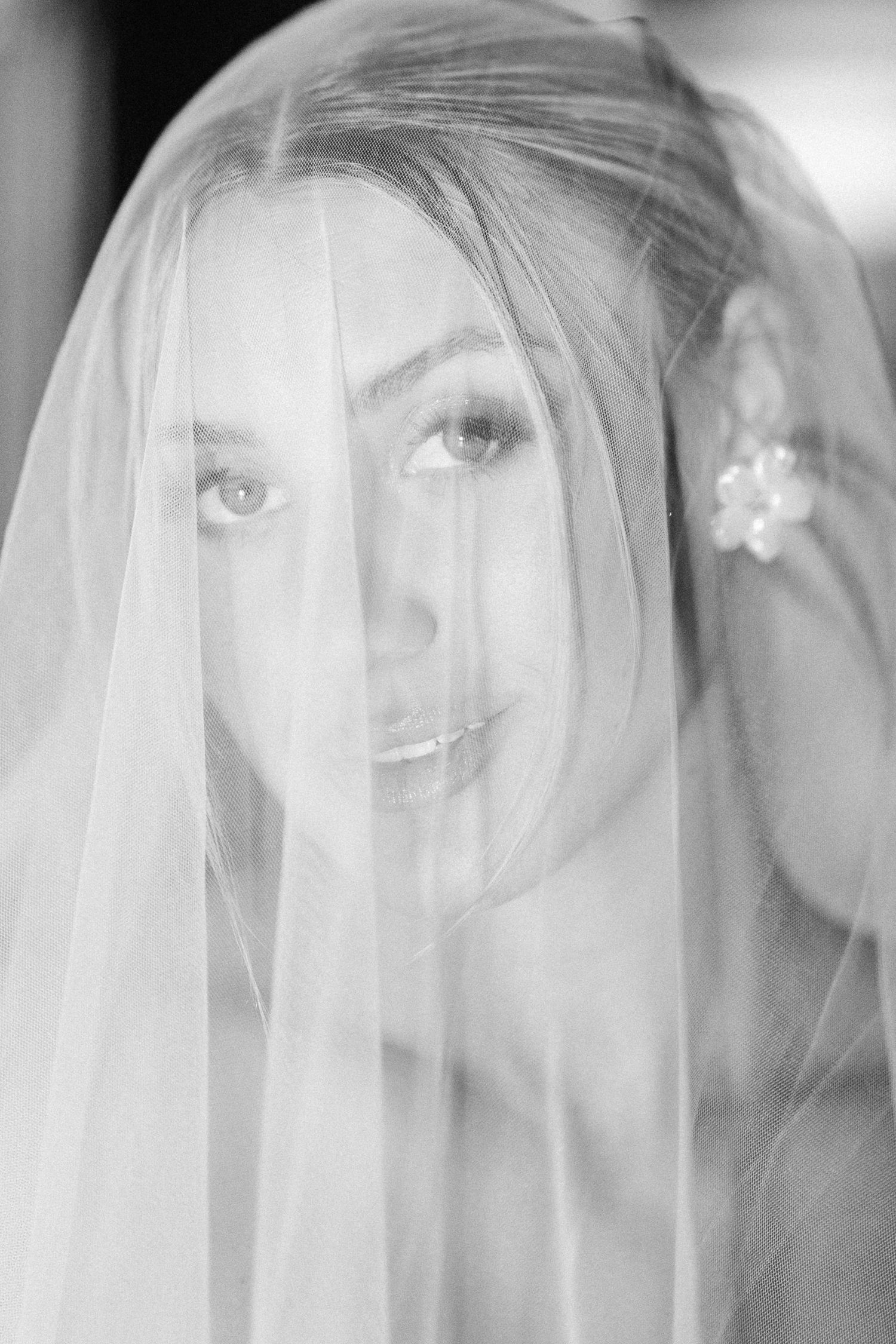 Ethereal black and white portrait of bride under delicate veil with soft lighting.