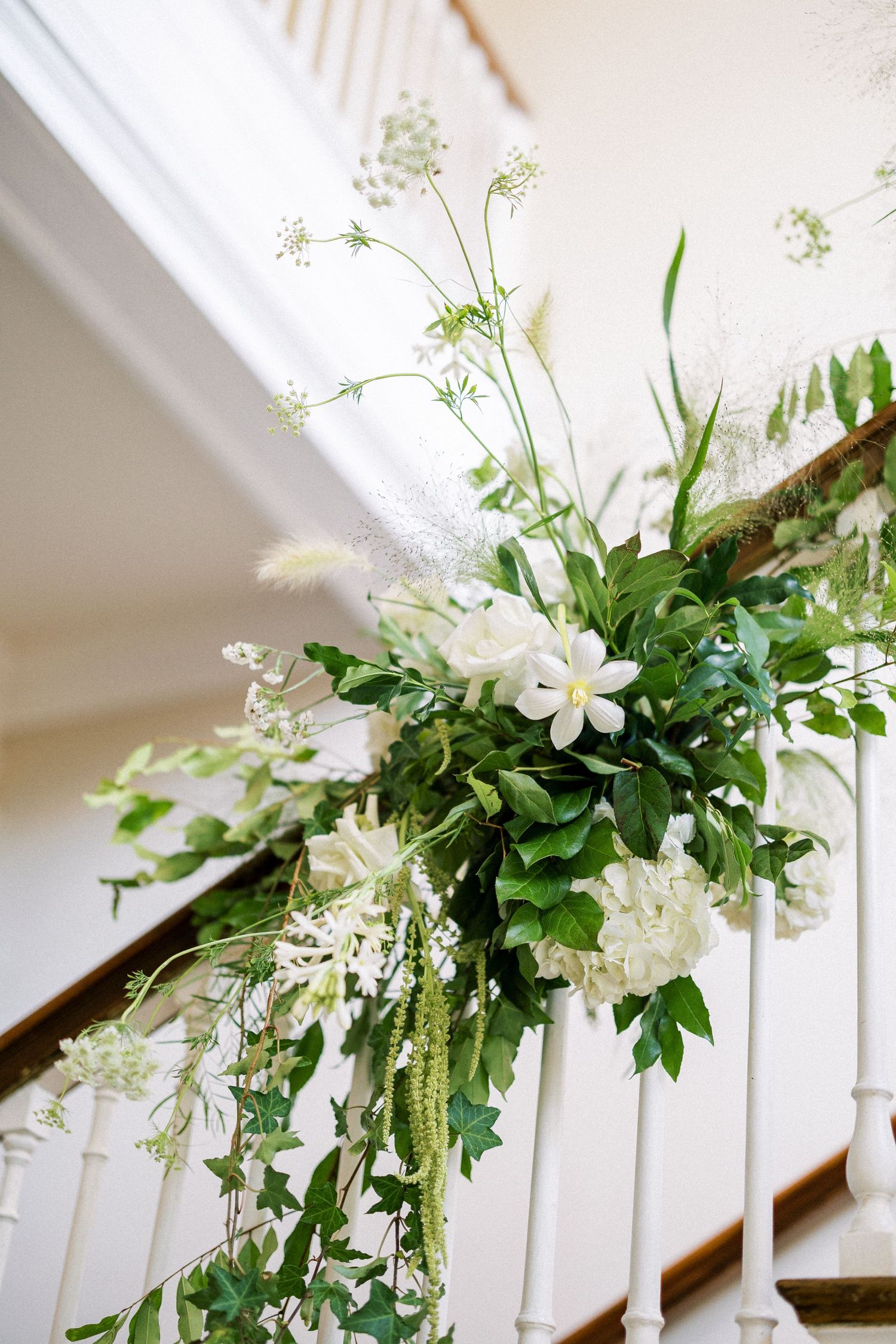 White floral staircase arrangement with delicate greenery cascading along white banister.