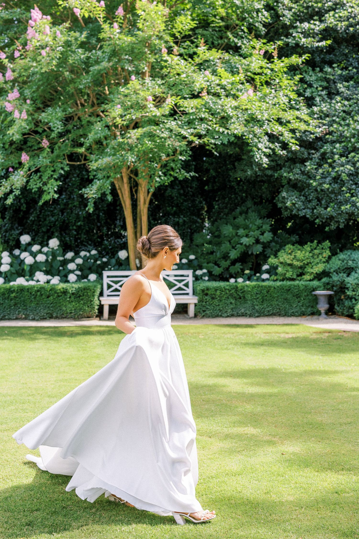 A flowing white dress twirls gracefully in a lush garden setting with a white bench in the background.