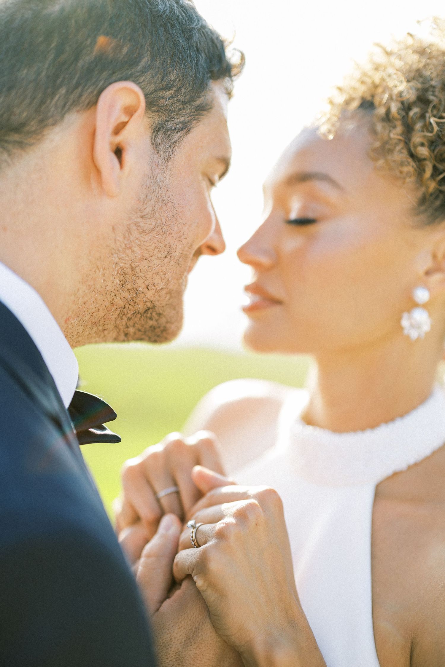 Close-up of a tender moment between newlyweds as they hold hands and lean in close together.
