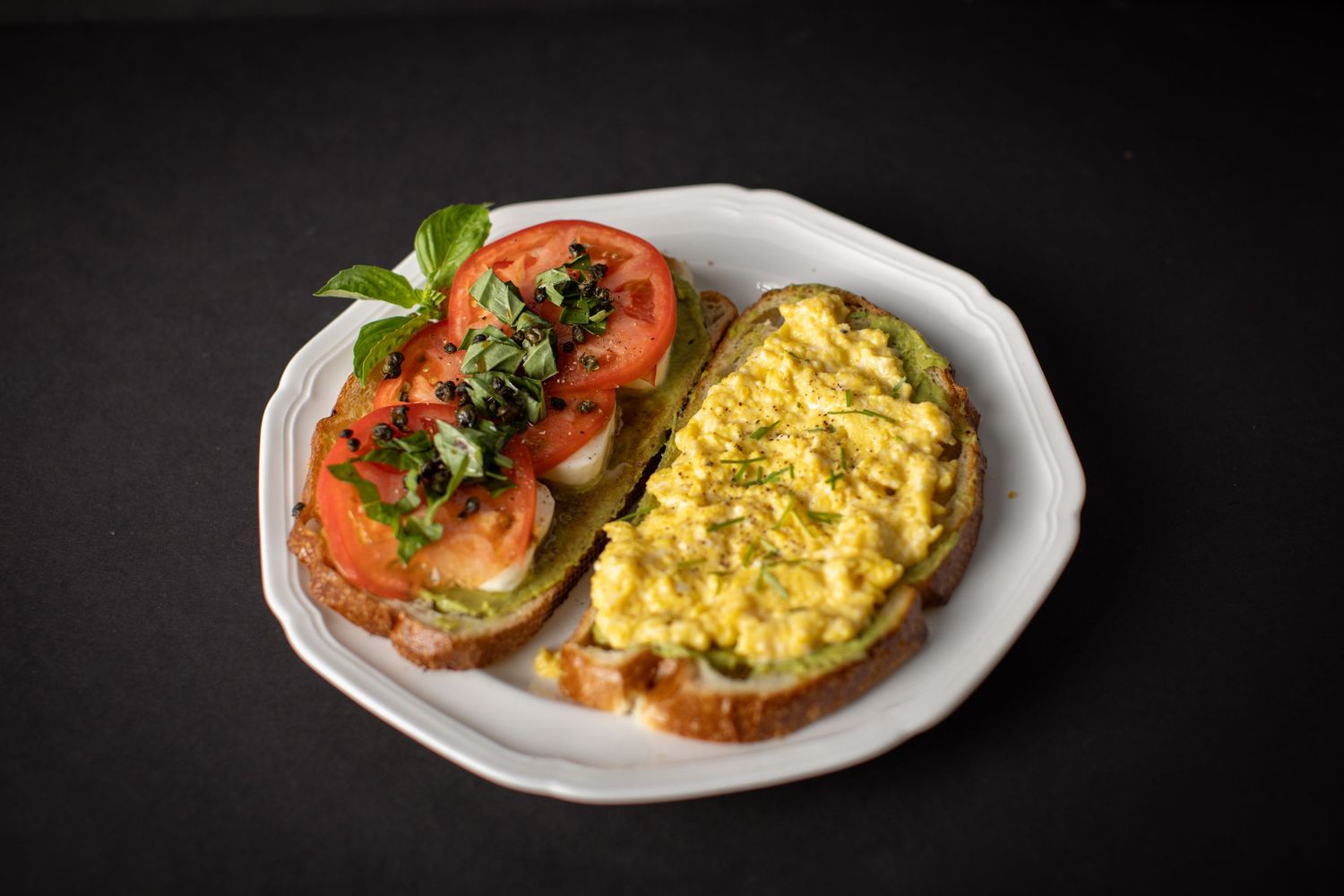 A breakfast plate with scrambled eggs and sliced tomatoes garnished with fresh herbs on white ceramic dishware.