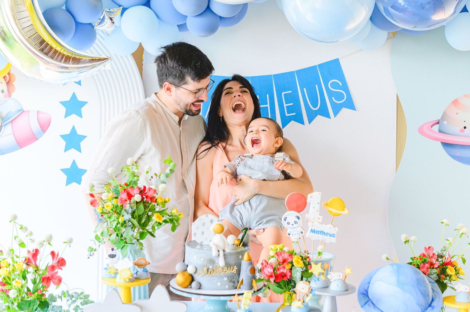 Joyful family celebrates with blue balloons, flowers and cake at a baby-themed party with star decorations.