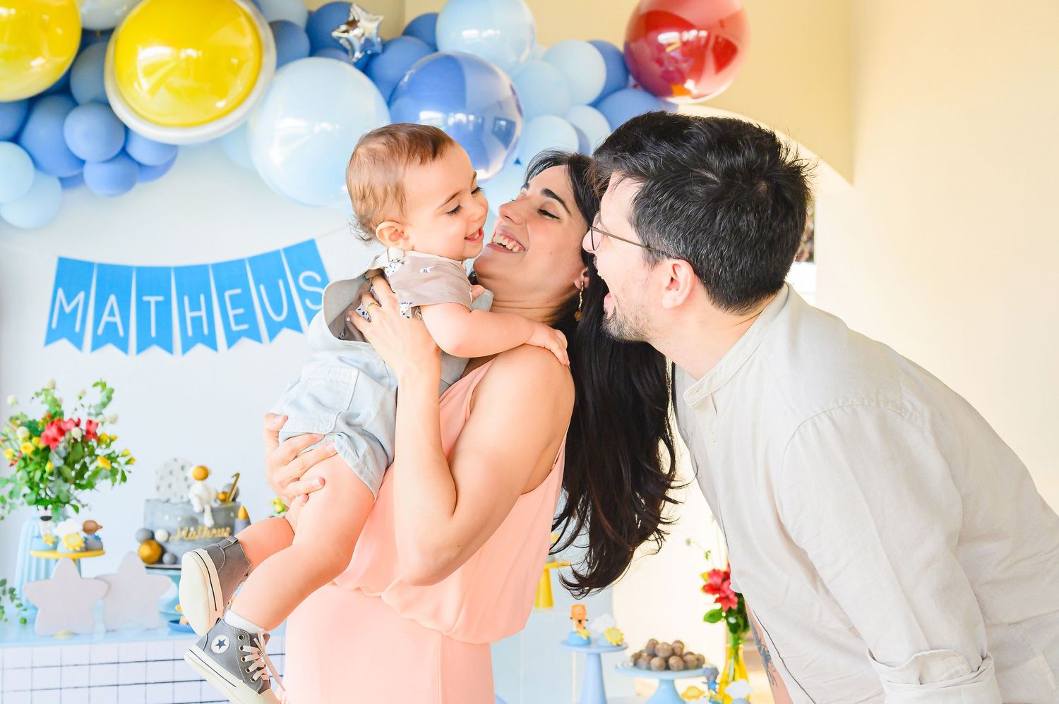 Happy family celebrates at a baby shower with blue balloons, flowers and yellow decorations in background.