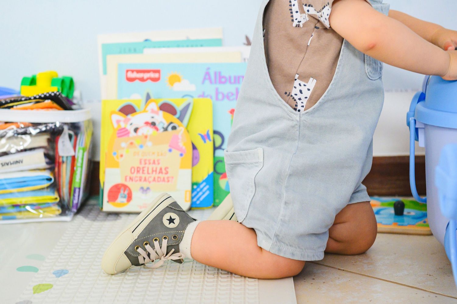 Children's books and a gray Converse sneaker sit on a tiled floor near a collection of colorful learning materials.