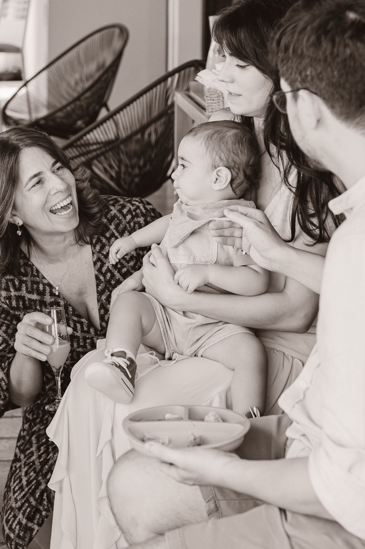 A candid black and white photograph showing a joyful gathering with a baby and friends sharing laughter and smiles.