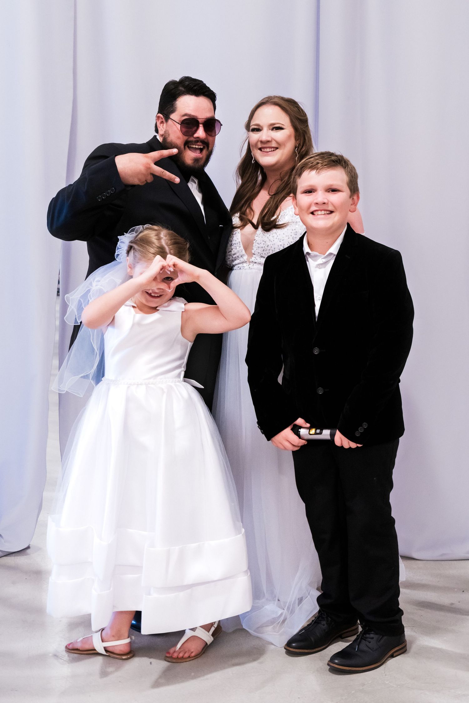 A family during a wedding, the father holding up the peace sign and the daughter holding a heart.