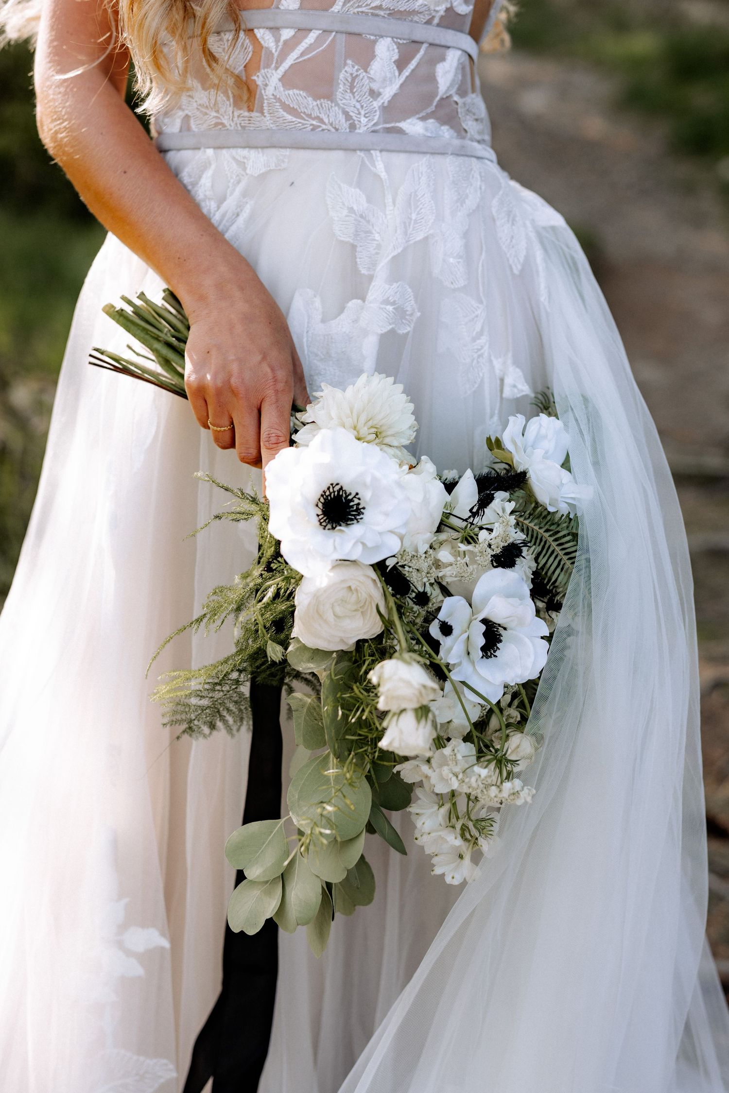 A delicate bridal bouquet of white anemones and roses is held against a flowing white wedding gown.