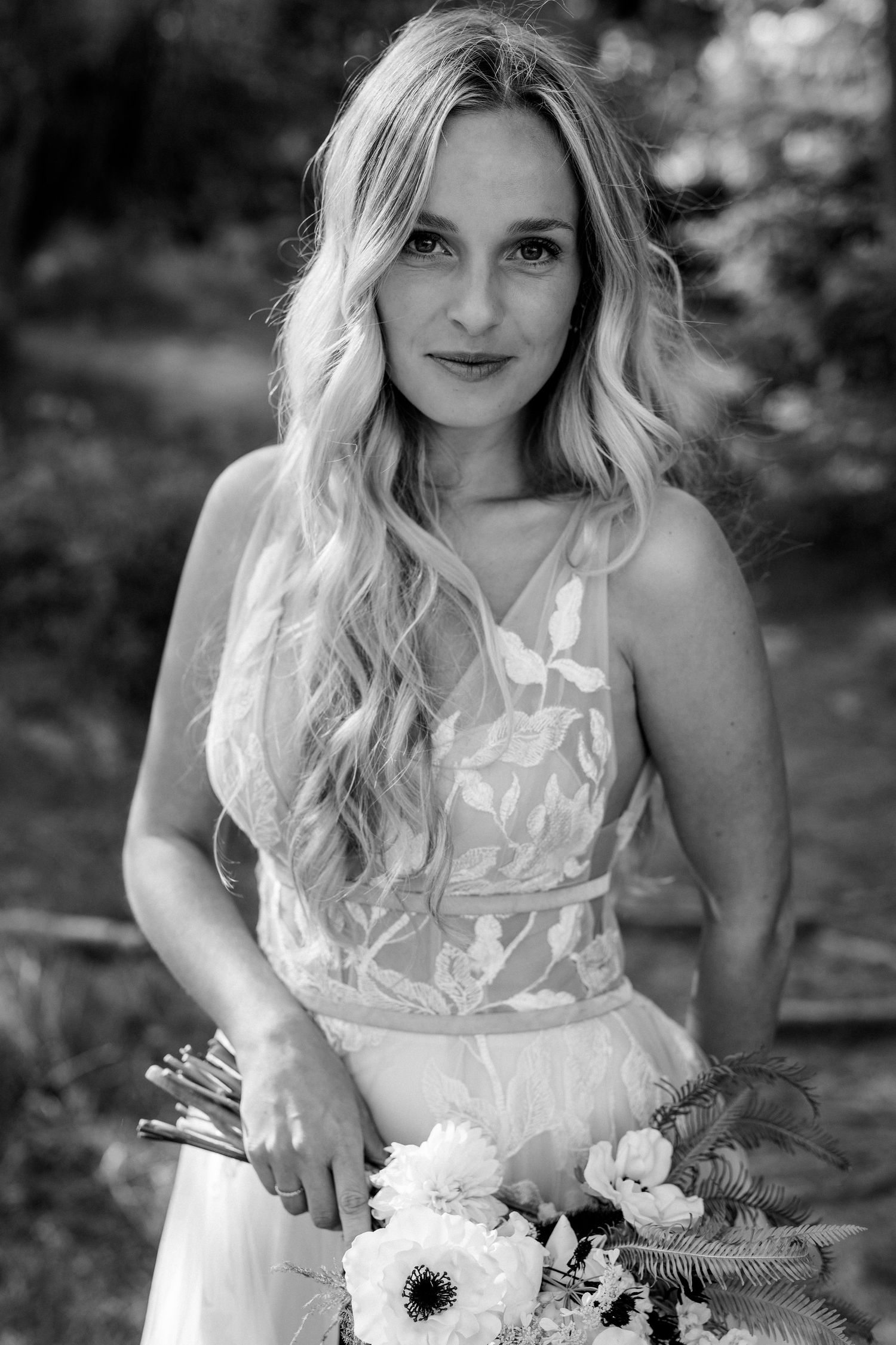 A black and white portrait photograph of a person in a white dress holding flowers outdoors.