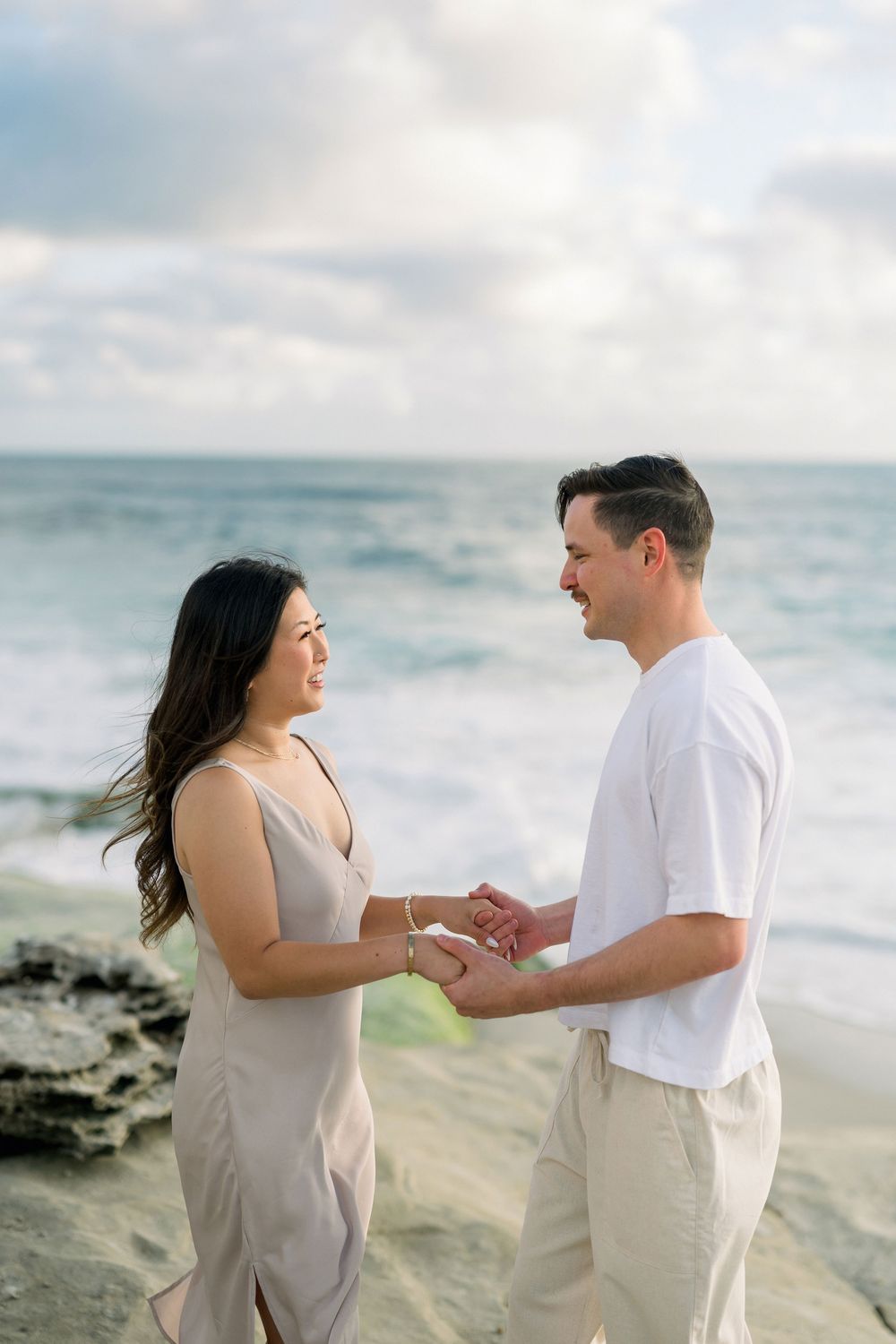 A romantic beach proposal moment with a couple holding hands against a backdrop of crashing waves.