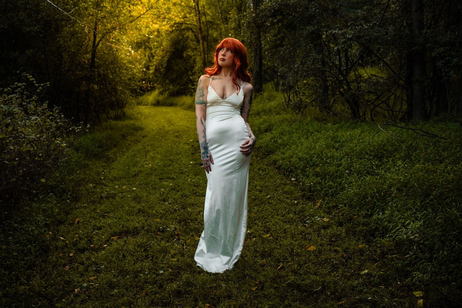 A figure in a white flowing dress and red hair stands on a mystical forest path illuminated by golden light.