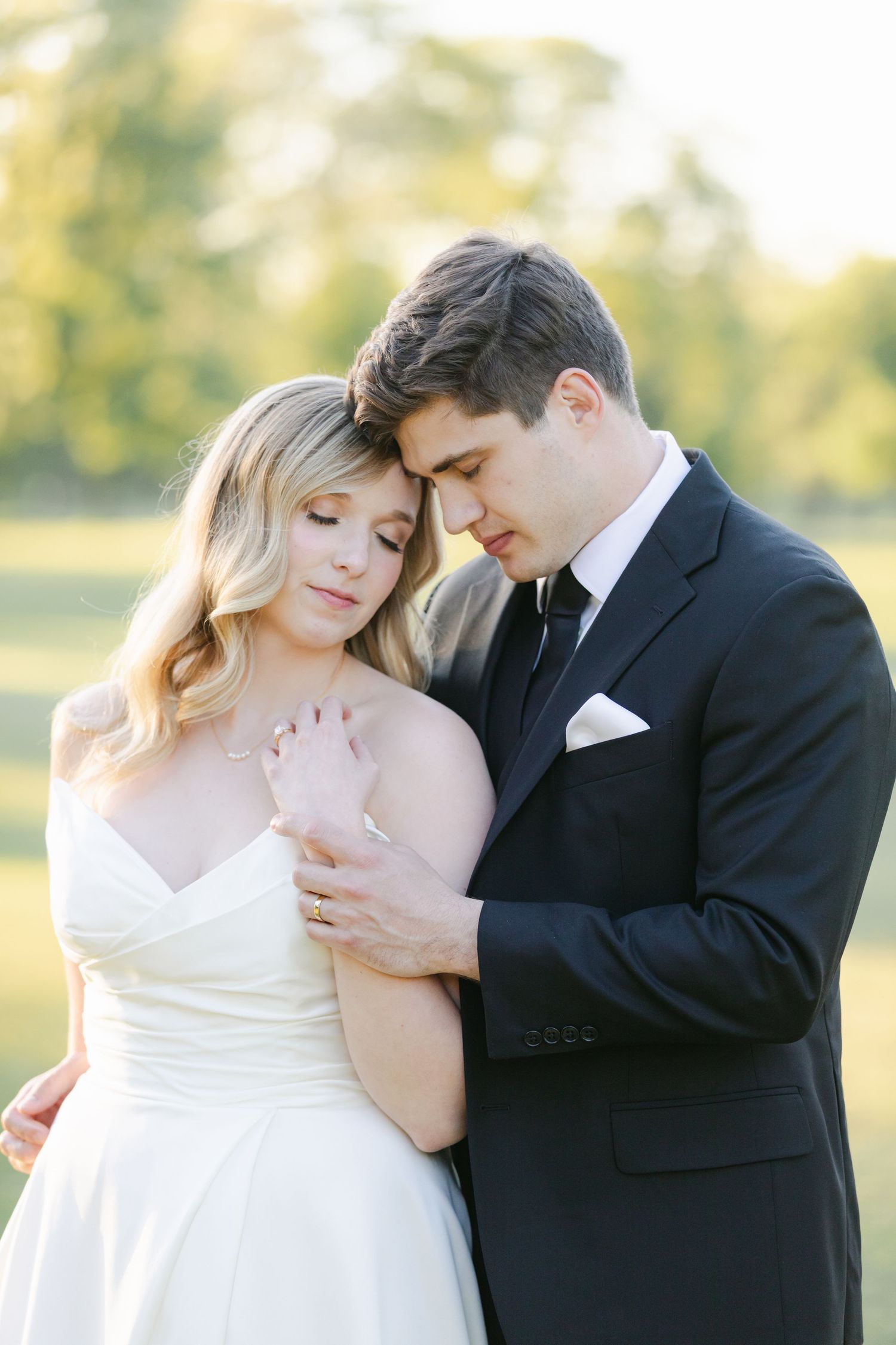 A romantic wedding portrait features a couple in formal attire sharing an intimate moment in a sun-drenched outdoor setting.