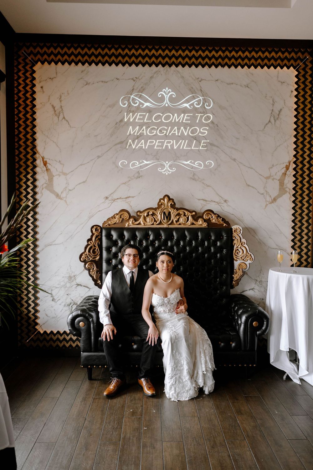 A couple sits together on an ornate black tufted loveseat beneath a welcome sign at Maggiano's Naperville.