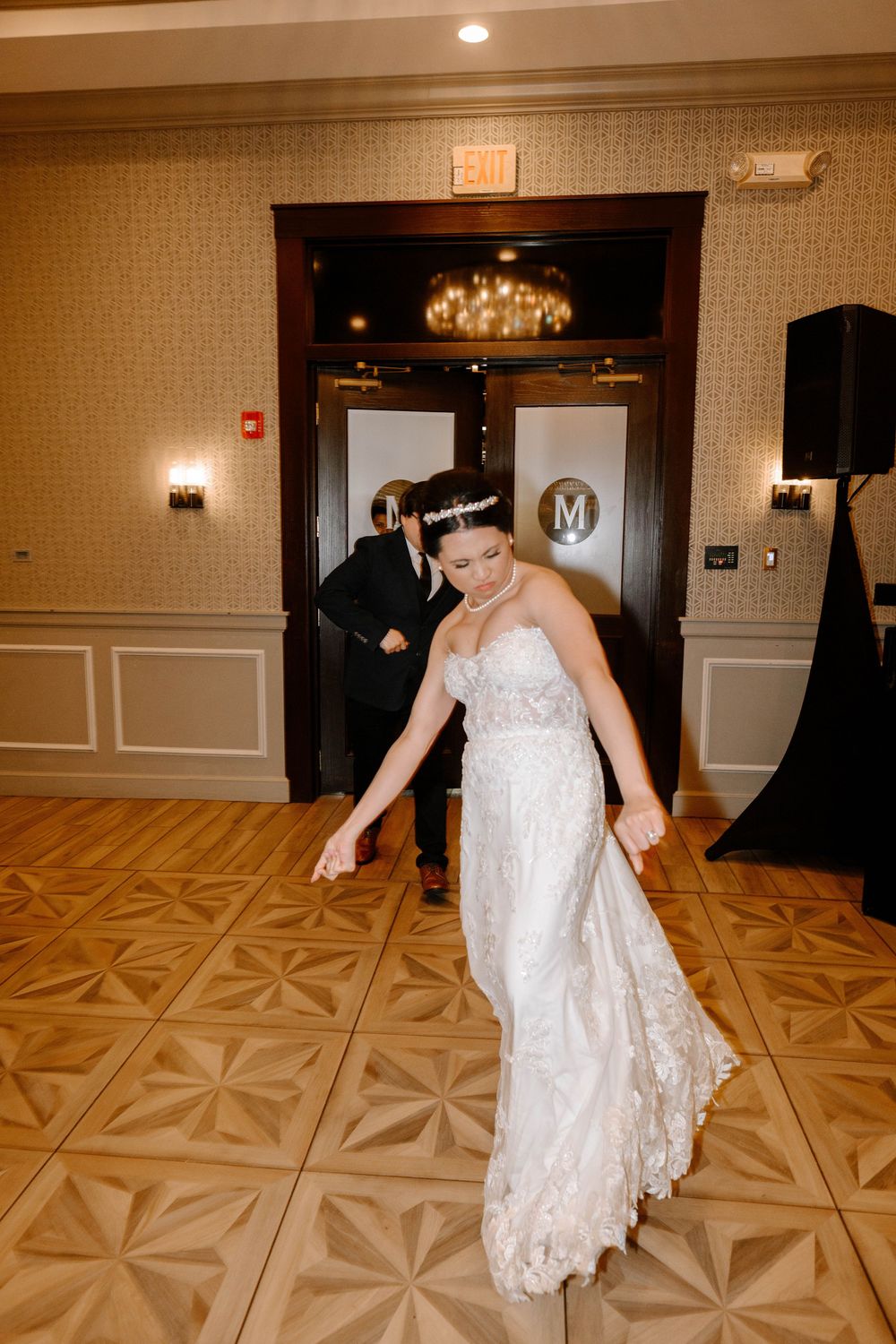 A wedding reception features a lace wedding dress on the dance floor beneath an elegant chandelier.