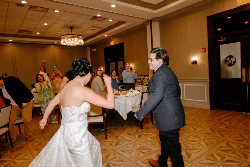 A couple dances together during a wedding reception in an elegant ballroom with patterned carpet and warm lighting.