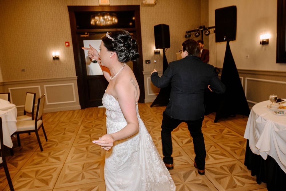 Couple dancing at a wedding reception in elegant ballroom with carpeted floor and speaker setup.