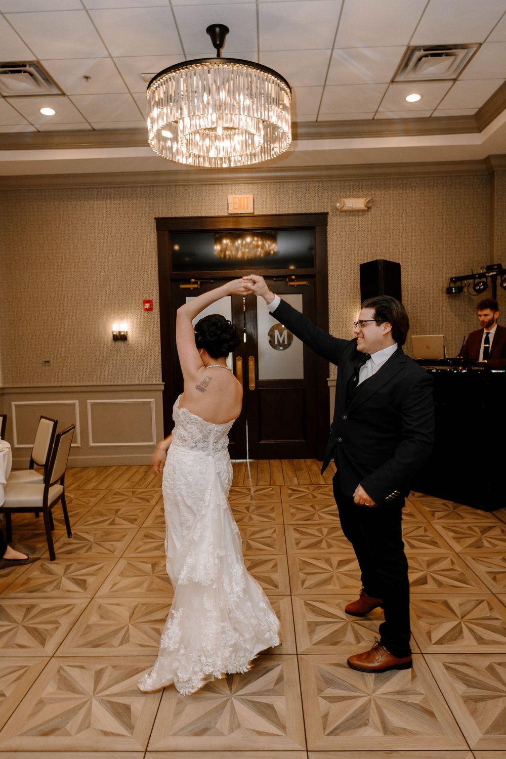 A couple dances together in an elegant ballroom beneath a crystal chandelier.
