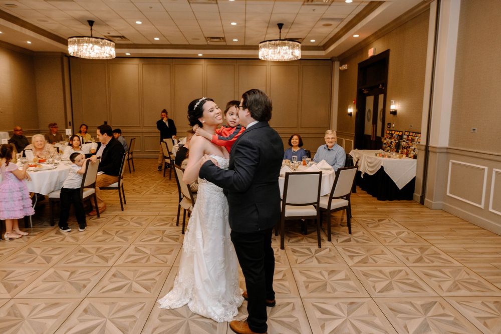 A couple shares their first dance together in an elegant hotel ballroom with round tables and soft lighting.