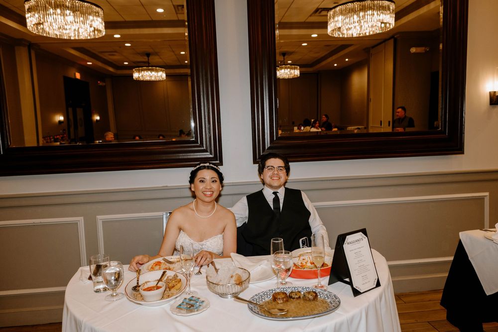 Elegant banquet hall dining setting with crystal chandeliers featuring a couple seated at a table with catered food.