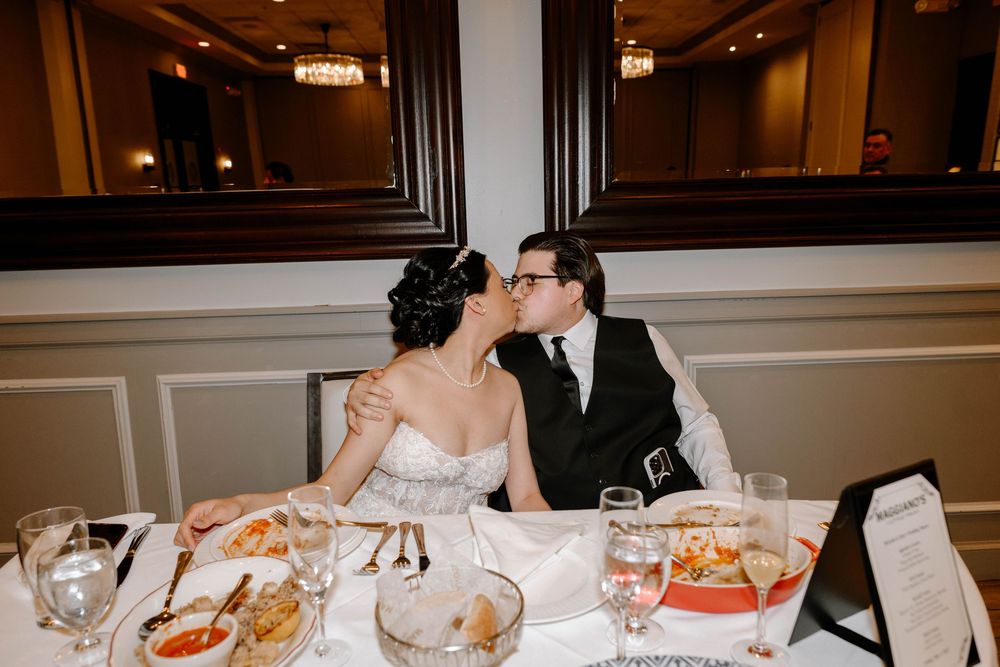 A couple shares an intimate moment at an elegant reception dinner table set with wine glasses and place settings.