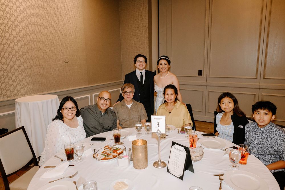 A group of people sit together at a round table during a formal dining event with white tablecloths and drinks.