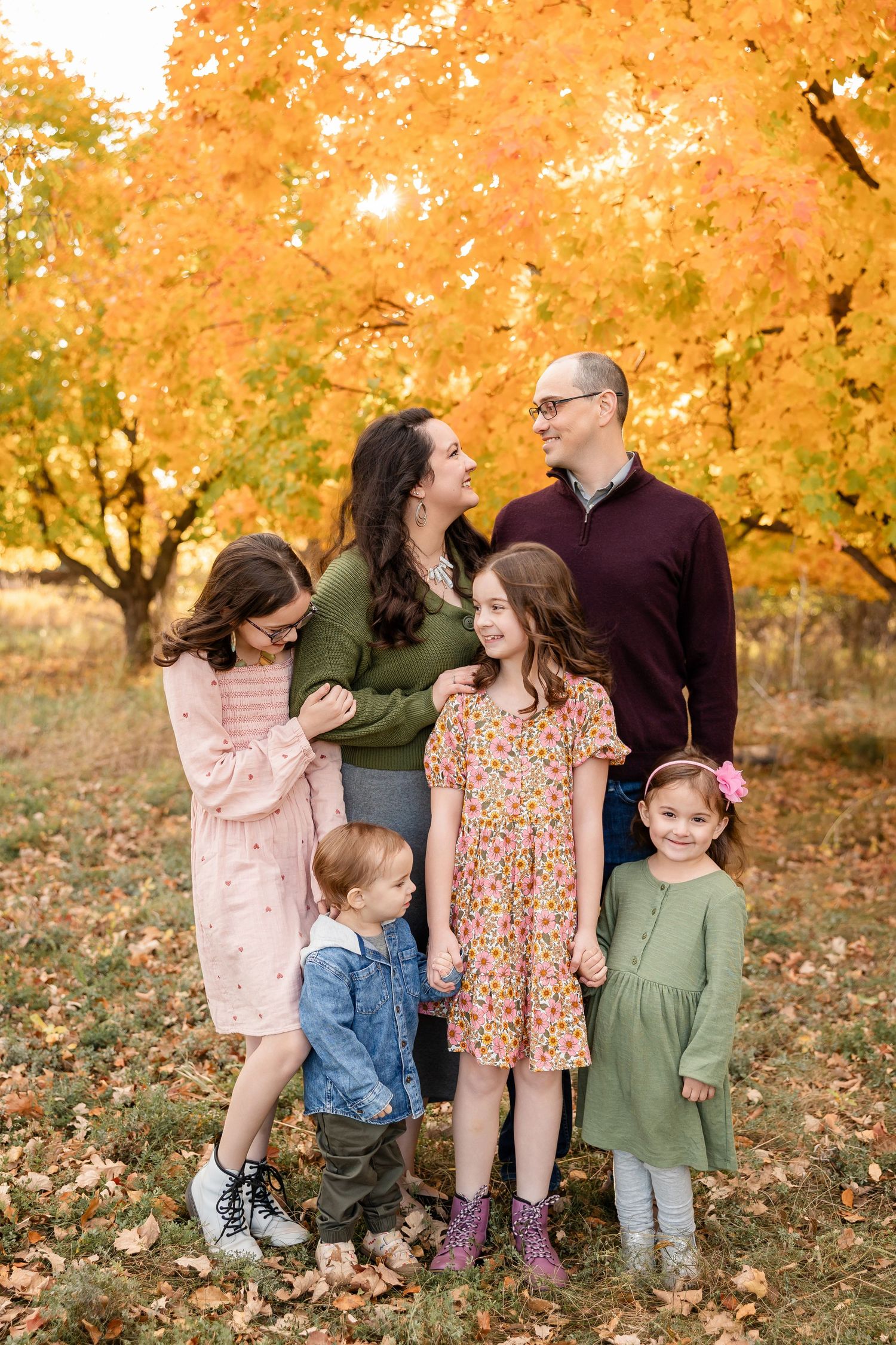 Family dressed in fall colors poses together beneath vibrant orange autumn maple trees on a crisp day.