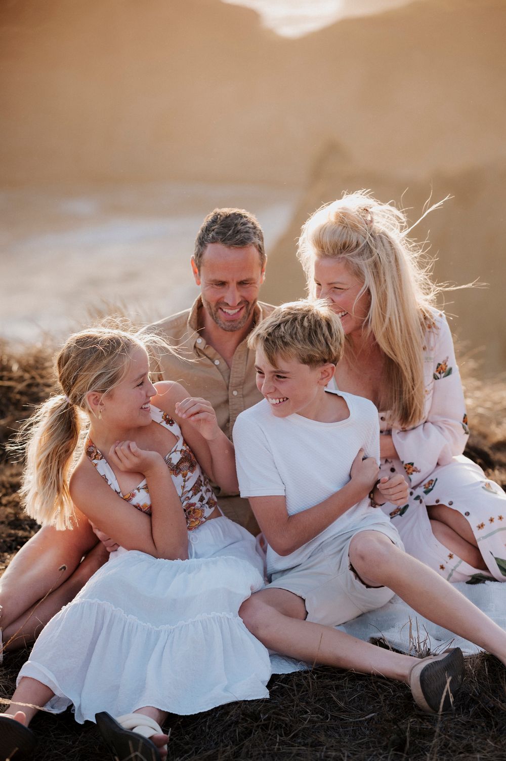 Family shares candid laughter while sitting together outdoors during sunset with mountains in background.