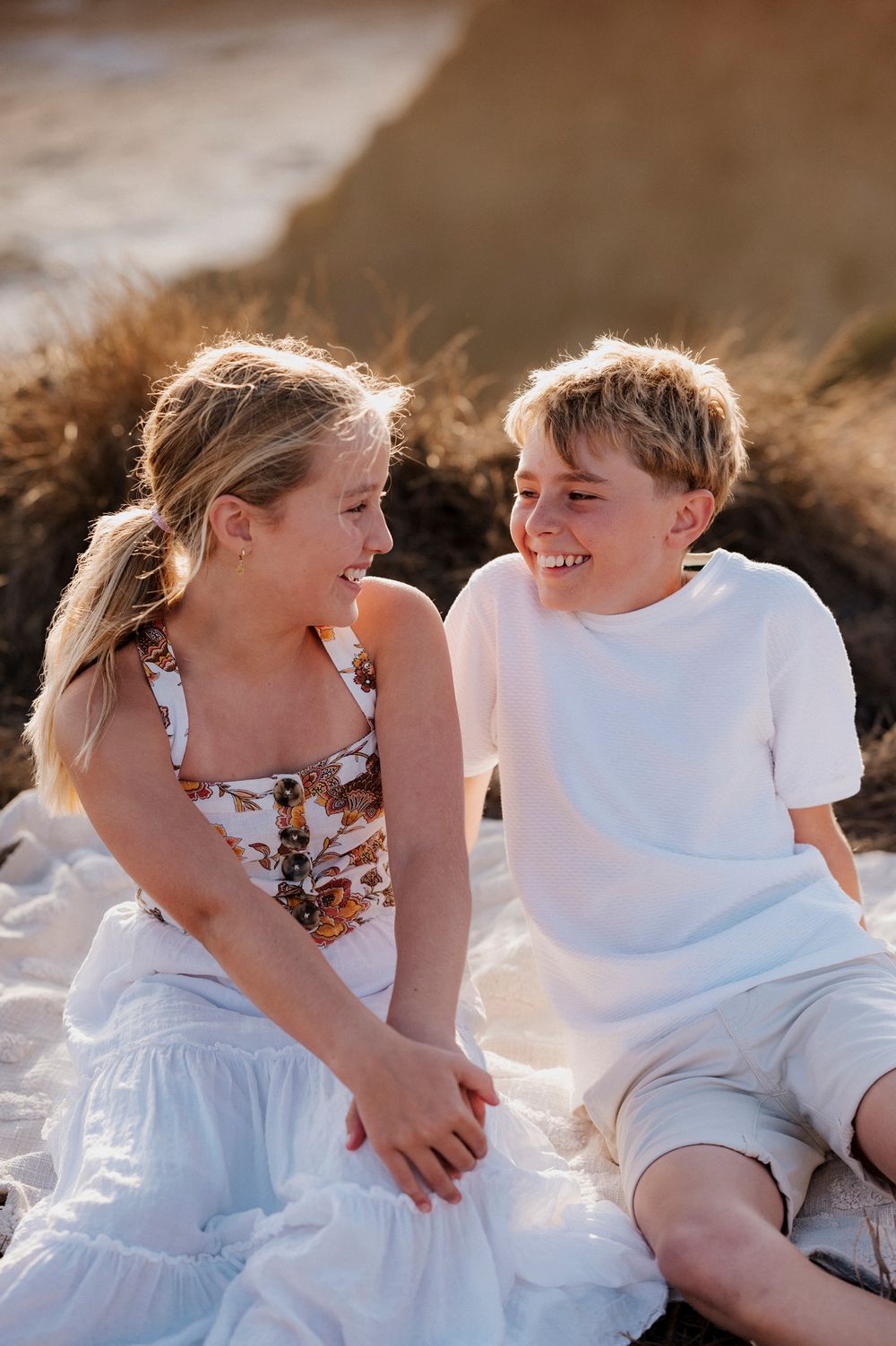 Two children laughing together while sitting outdoors in warm sunlight during golden hour.