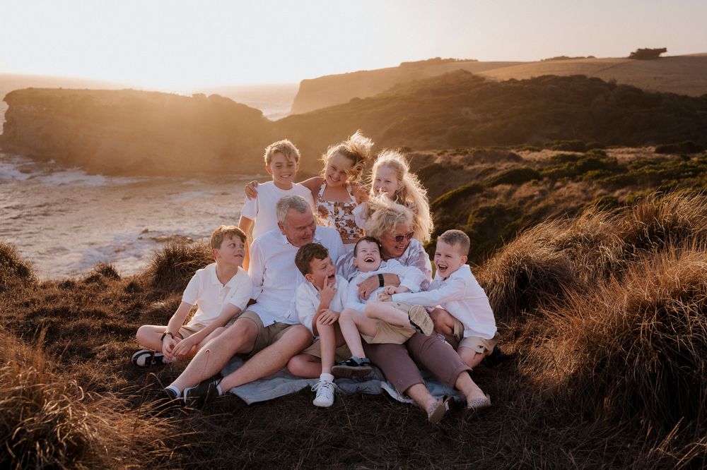 A group in white clothes sits together on a coastal cliff at sunset creating a warm family portrait moment.